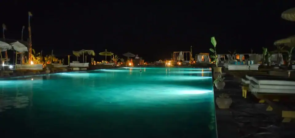 Luxurious swimming pool at Marrakech Stay Vip resort illuminated at night, offering a tranquil retreat with elegant lounge chairs and exotic decor for an unforgettable Moroccan vacation.